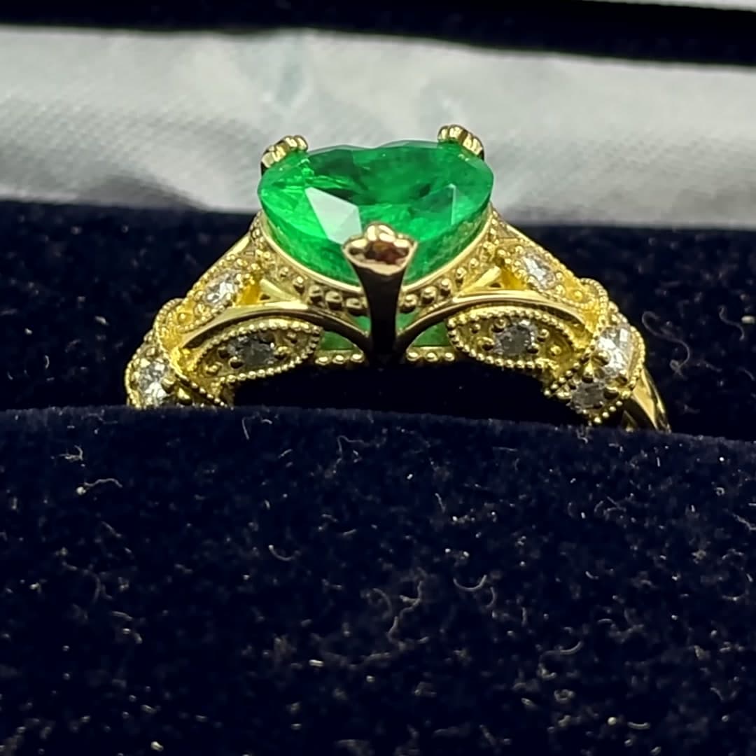 Anillo de oro con una esmeralda talla corazón y hombros de diamantes, en su estuche de terciopelo azul