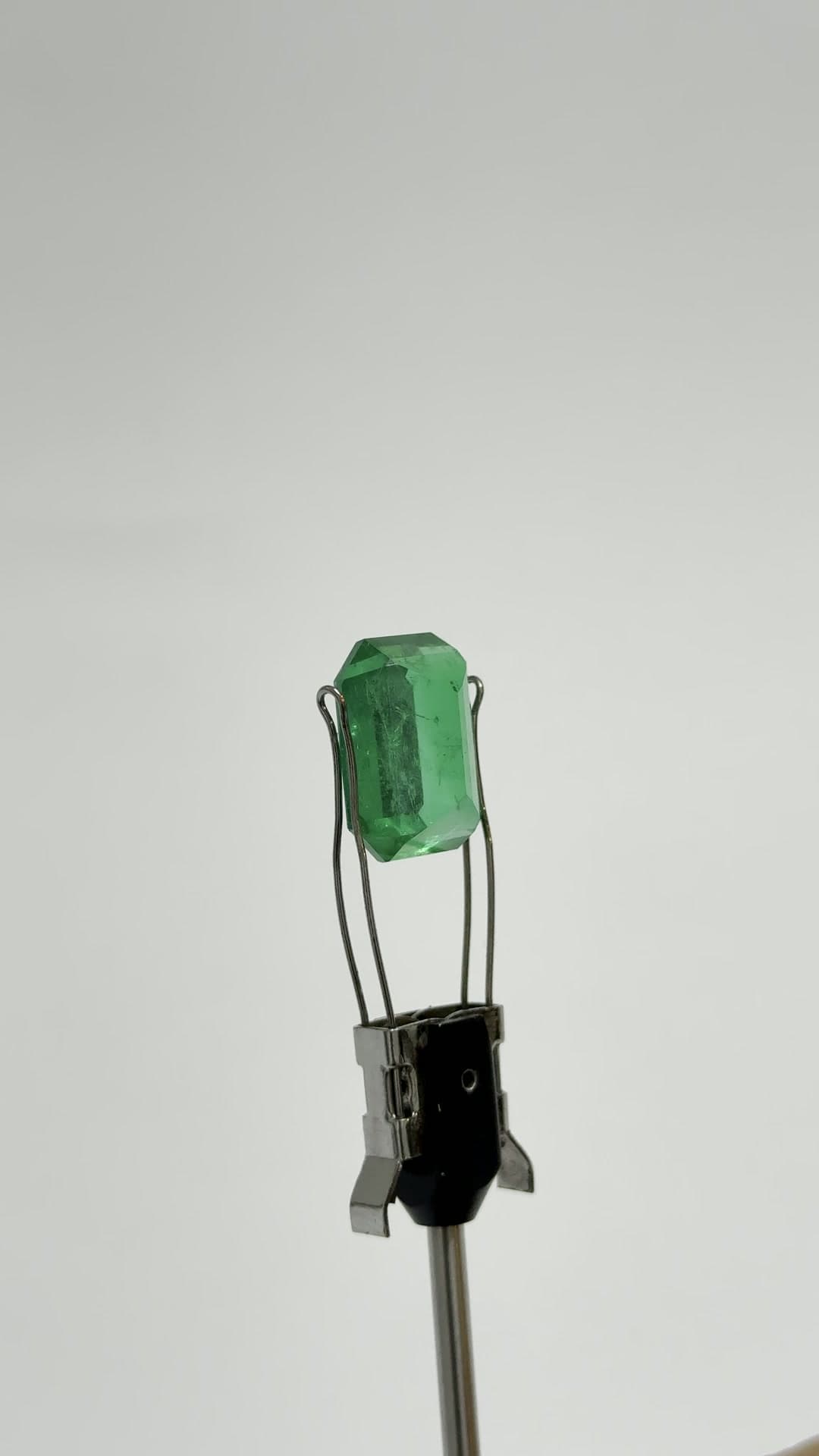 Un cristal de esmeralda en bruto sujeto en una pinza de estudio, sobre fondo gris